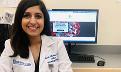 Dr. Sarah Mushtaq sits in front of a computer showing the Covid-19 and Cancer Consortium homepage